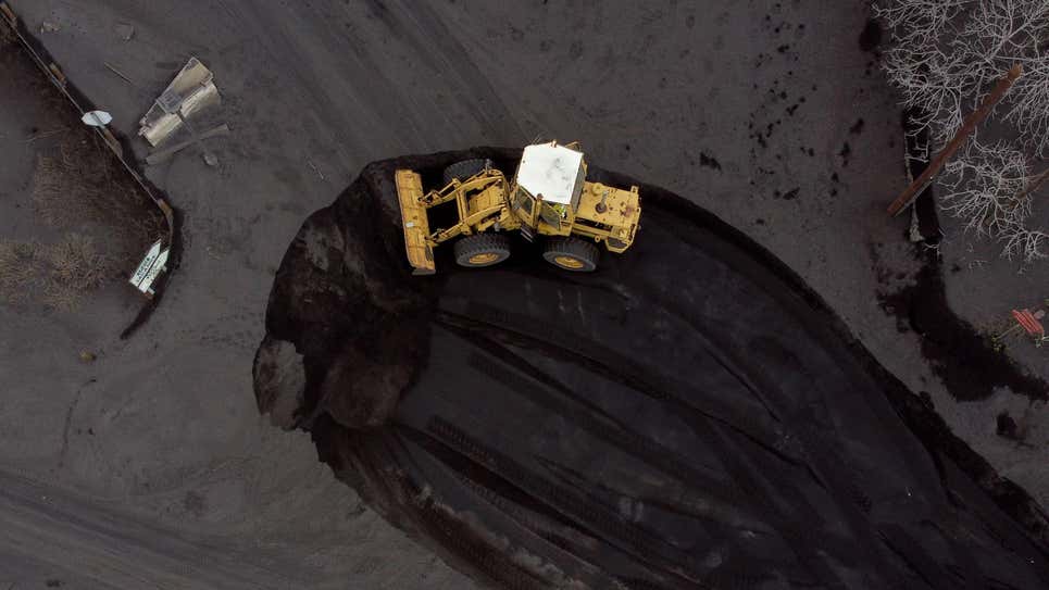 Una excavadora remueve cenizas de una calle cubierta de ceniza y lava por la actividad del volcán.