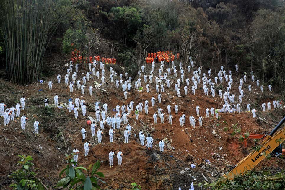 Esta foto, tomada el 27 de marzo de 2022, muestra a los rescatistas de pie en un tributo en silencio por las víctimas en el lugar del accidente aéreo de China Eastern Airlines en el condado de Tengxian, ciudad de Wuzhou, en la región sureña de Guangxi en China. - El Boeing 737-800 volaba entre las ciudades de Kunming y Guangzhou el 21 de marzo cuando cayó en picado contra la ladera de una montaña, se desintegró en el impacto y mató a las 132 personas a bordo.