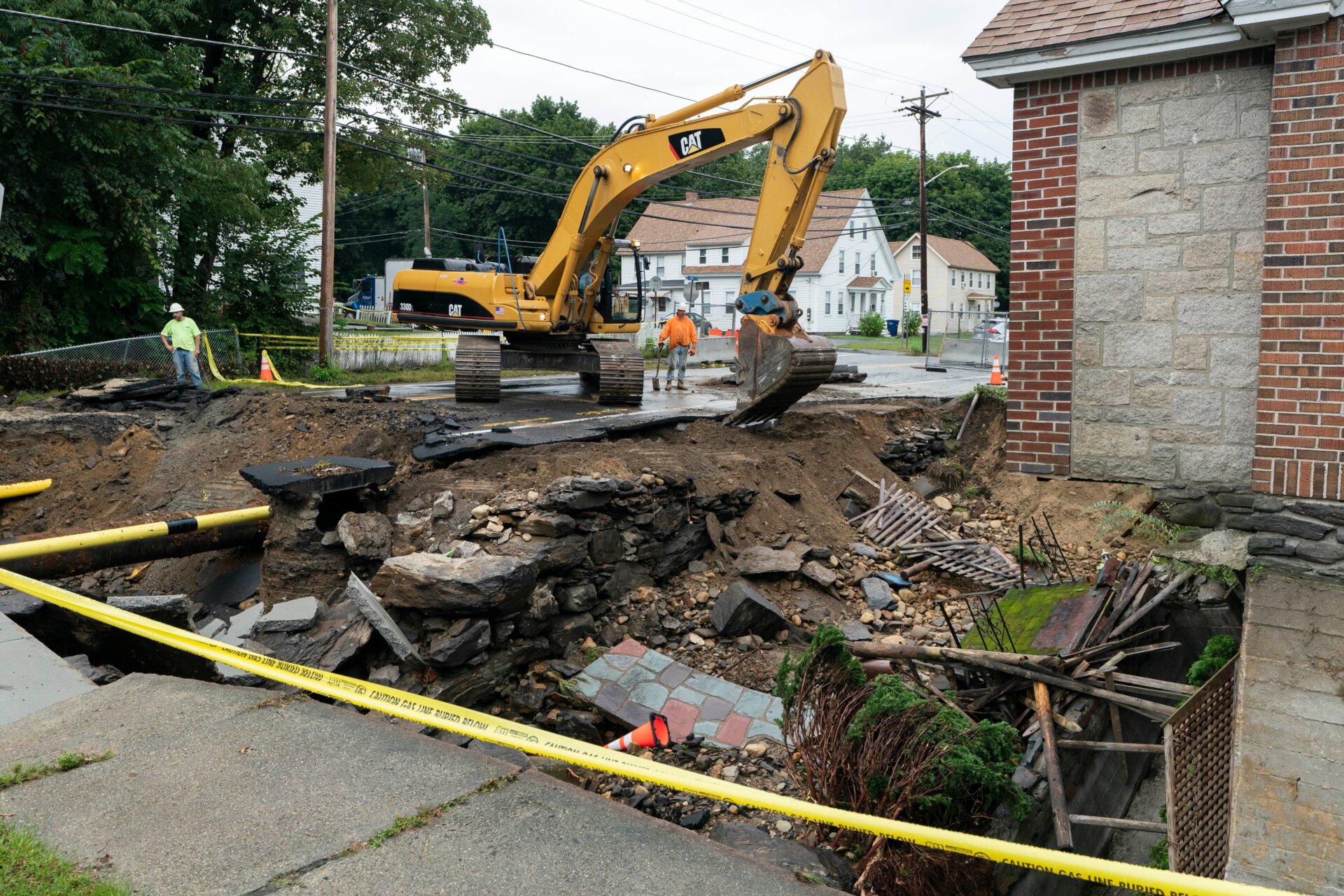 Una excavadora remove una acera enfrente de una casa donde el patio delantero y la carretera fueron arrasados por una inundación reciente, en  13 de septiembre de 2023, en Leominster, Massachusetts. 
