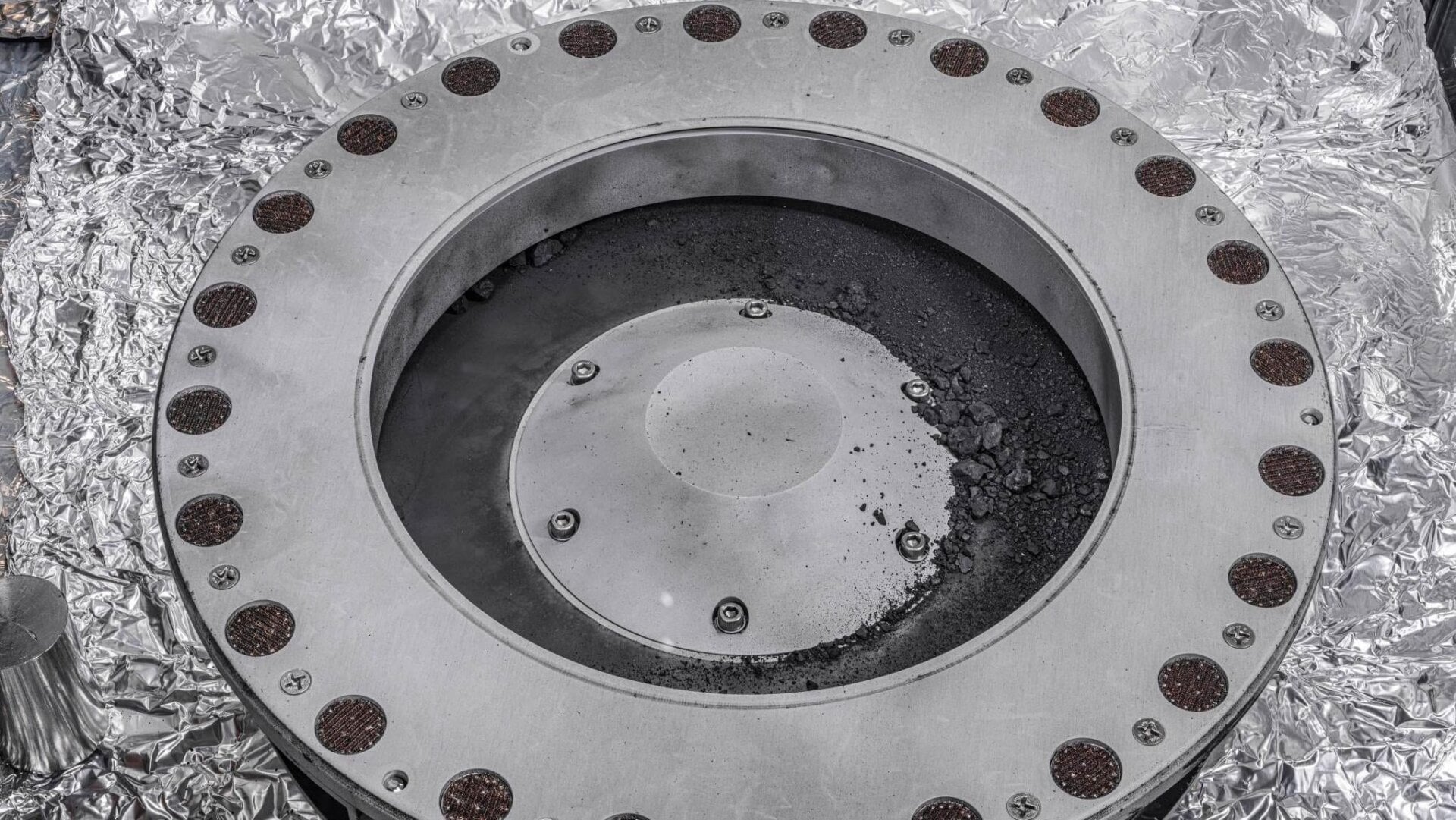 Escombros del asteroide Bennu en el exterior del recolector de muestras OSIRIS-REx.