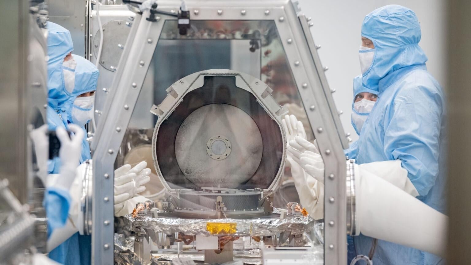 Miembros del equipo de curación de la NASA junto con especialistas en recuperación de Lockheed Martin quitando la tapa del recipiente.