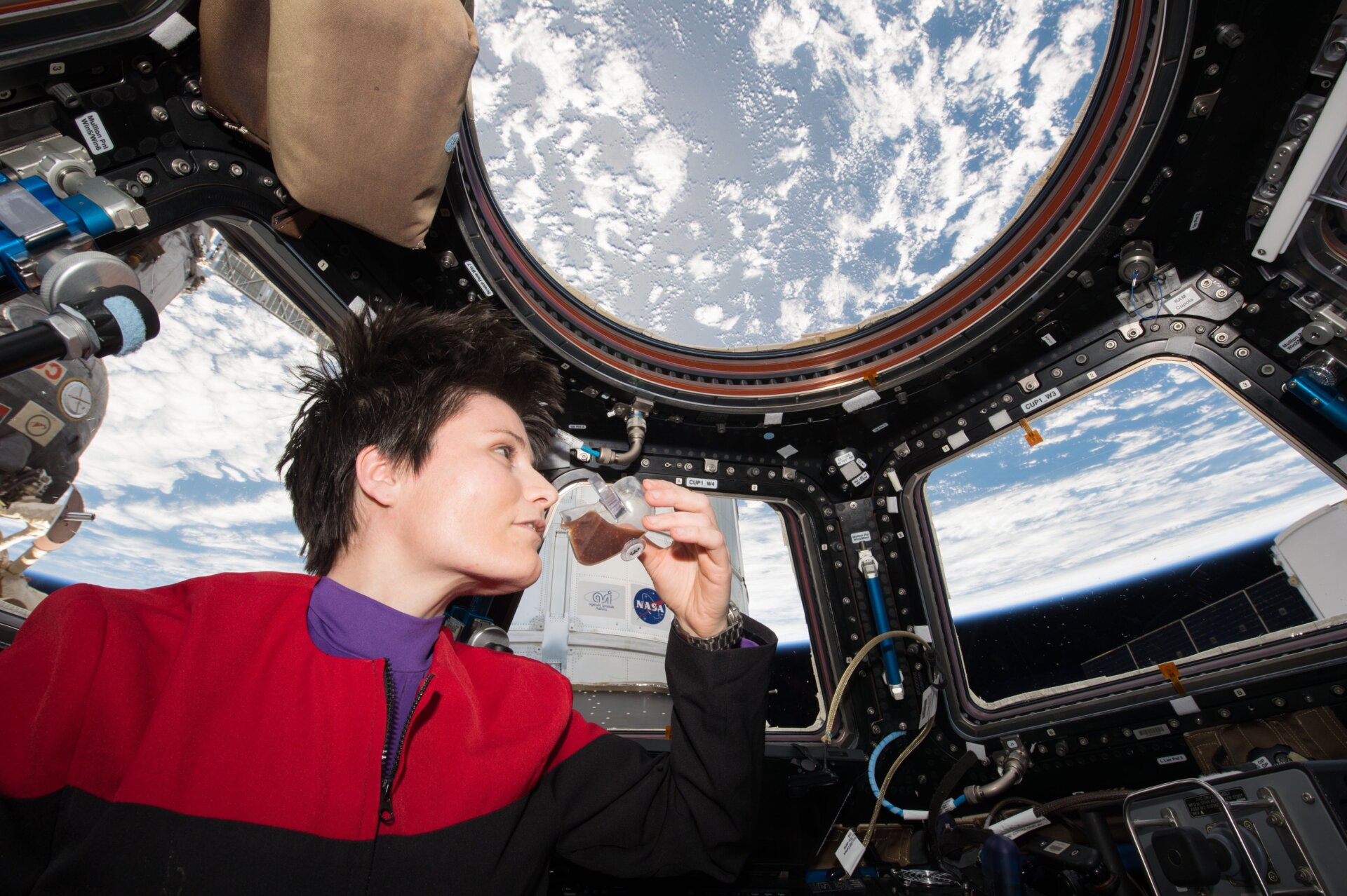La astronauta de la Agencia Espacial Europea (ESA) Samantha Cristoforetti, vistiendo un uniforme inspirado en el Star Trek: la Voyager serie, disfruta de una taza de espresso mientras mira por la ventana de la cúpula a bordo de la ISS.