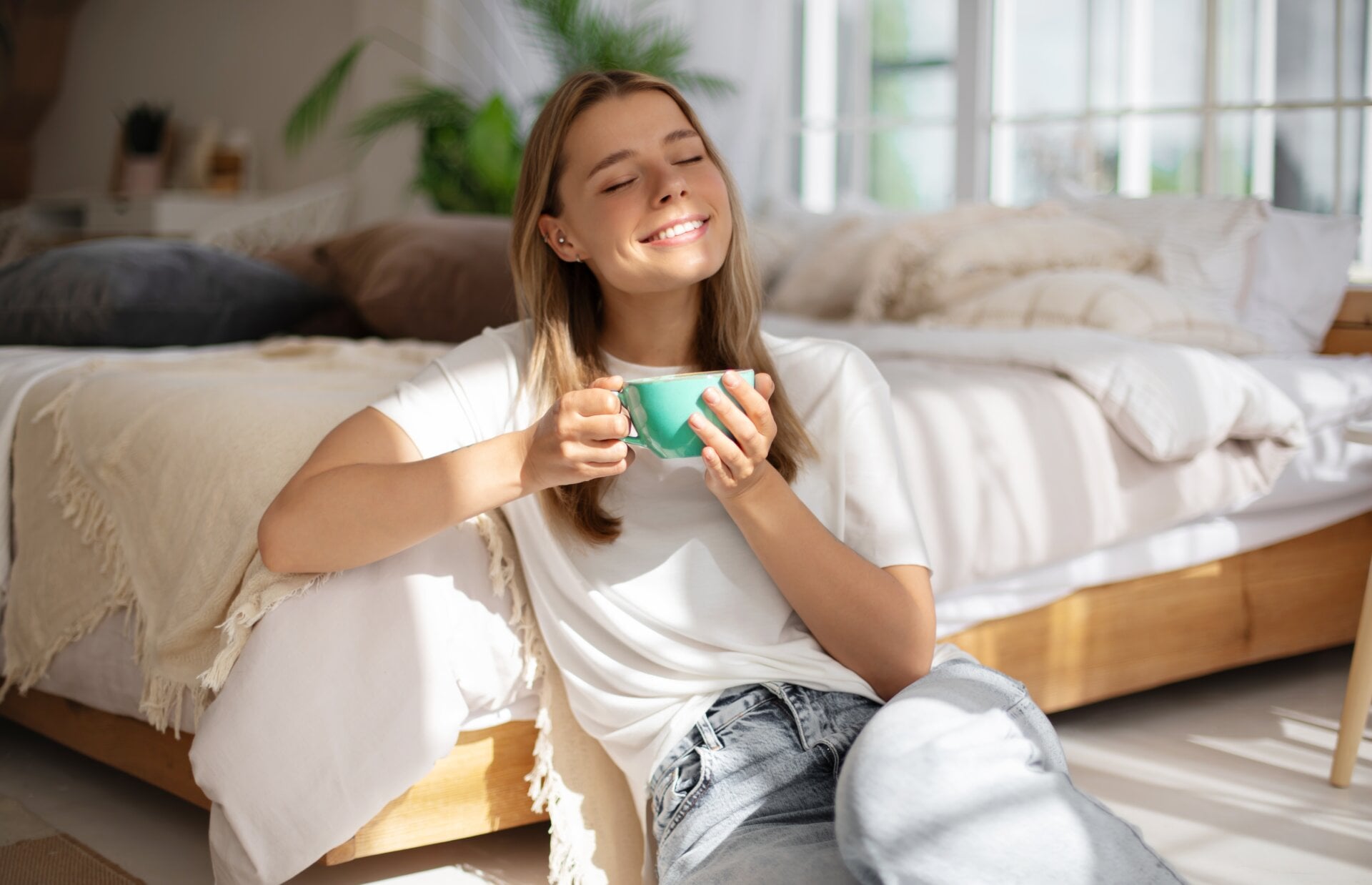 Young,woman,relaxes,in,sunlight,,holding,teal,mug,with,eyes
